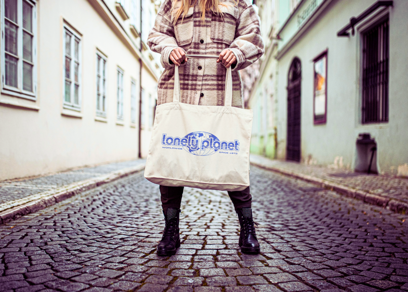 Lonely Planet Merch by TVP Tote Bag held by a model on a cobbled street