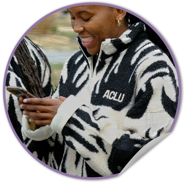 Person wearing a zebra-patterned TVP NYC produced jacket with 'ACLU' logo, holding a phone.