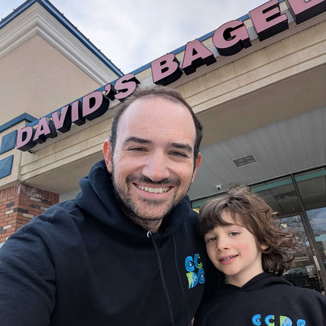 Omri Bojko, Co-Founder of TVP NYC and Total Commerce Partners. Omri is standing with his son wearing the same swag in front of a David's Bagels shop.