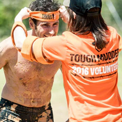 A Tough Mudder endurance event competitor and volunteer. The competitor is wearing a Tough Mudder branded headscarf and the volunteer is wearing branded Tough Mudder shirt and cap. 