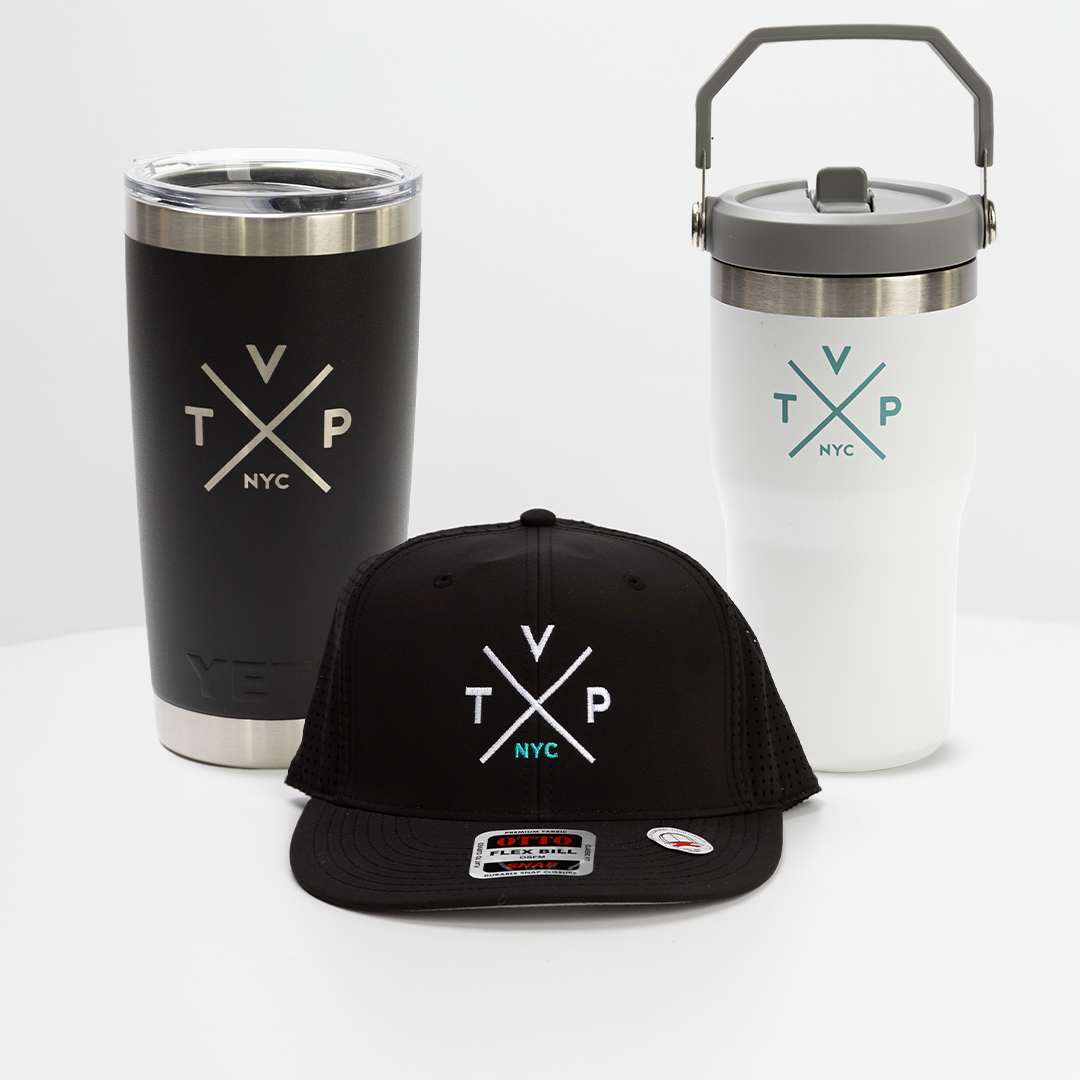 A professional product shot featuring a black YETI tumbler, a white insulated water bottle, and a black snapback hat, all featuring the signature TVP cross-logo.