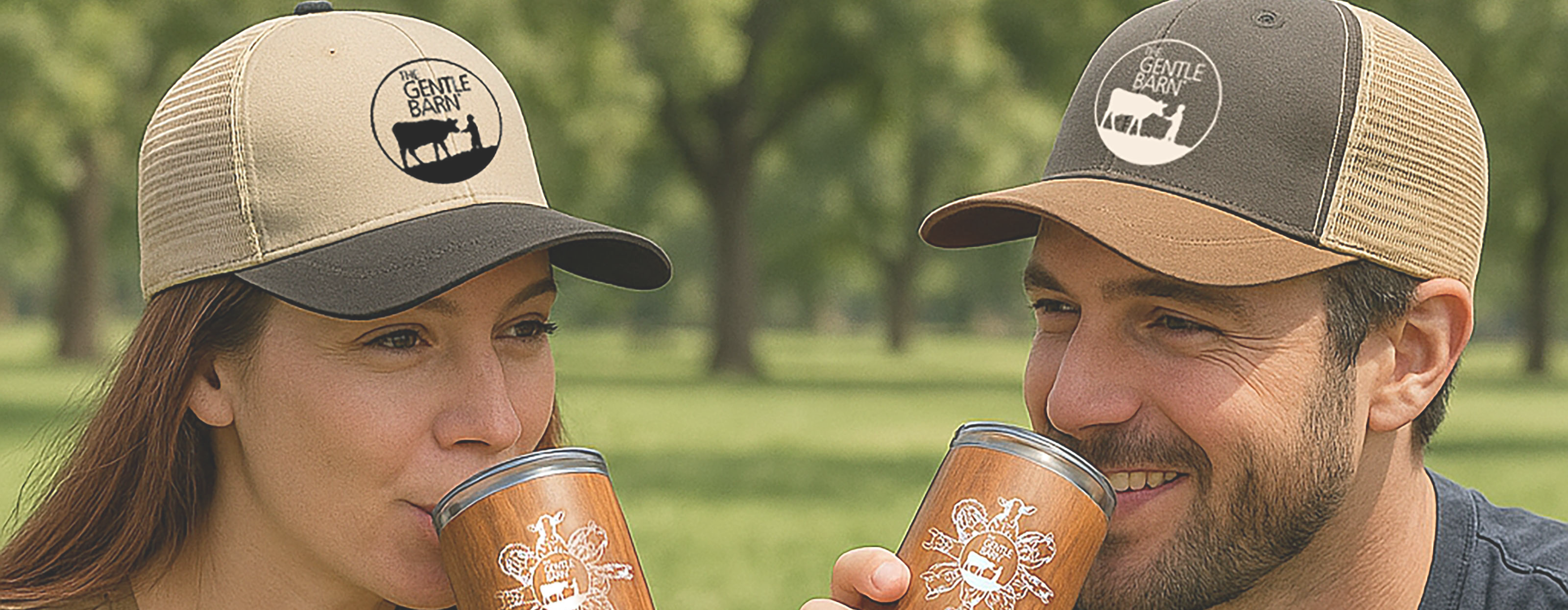 Two people wearing matching hats with a logo, drinking from insulated cups outdoors.